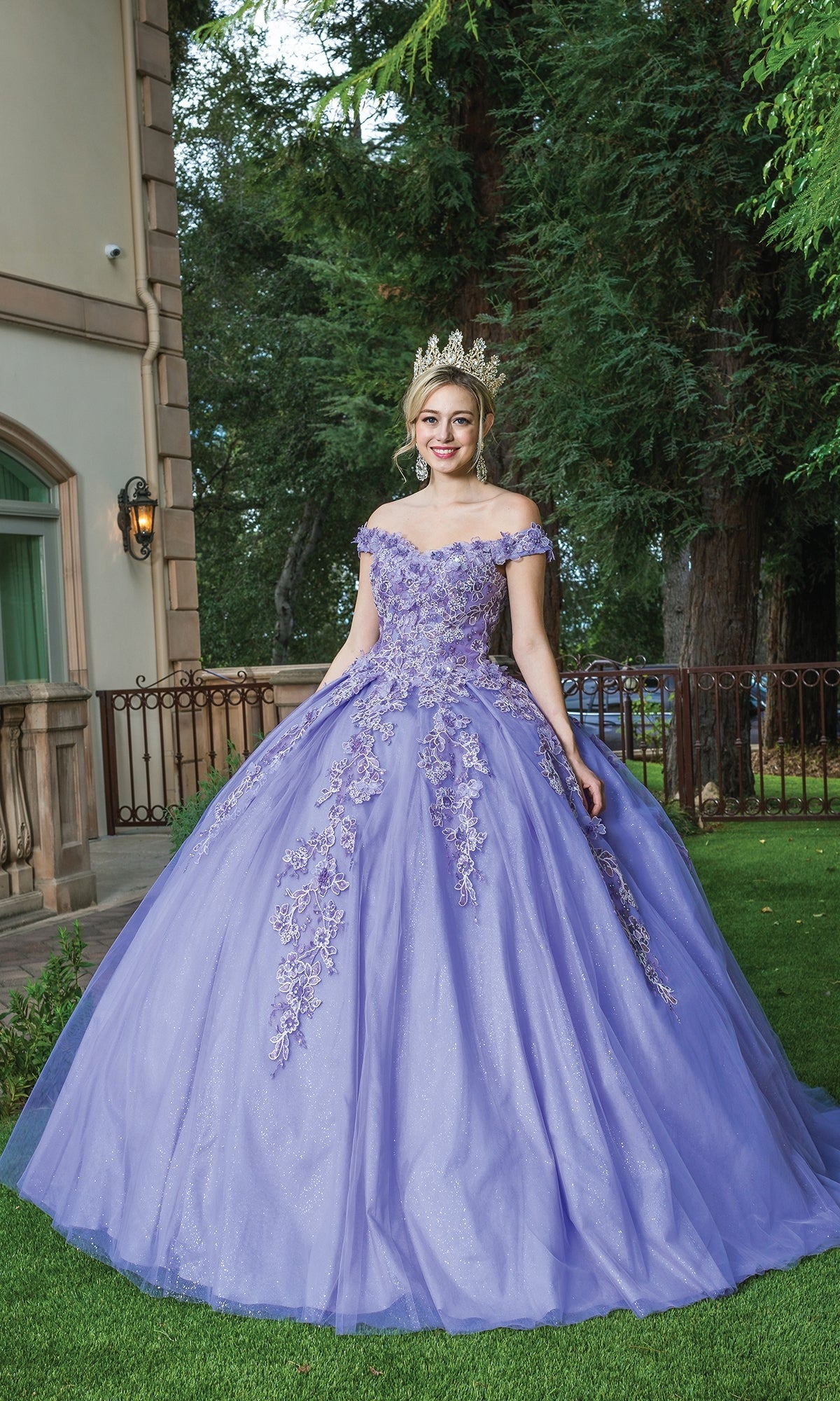 A young woman smiles at the camera while standing on grass outside a building, wearing the Quinceanera Dress 1574 by Dancing Queen, featuring a sweetheart neckline and floral embroidery.